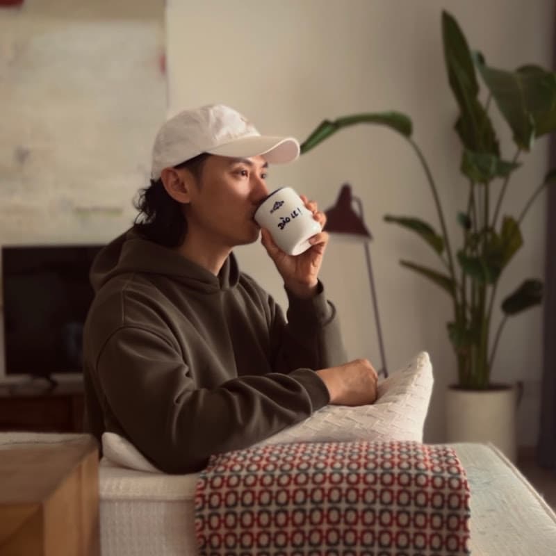 Johannes at home with a coffee, throw blanket over the sofa arm